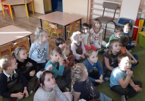 Dzieci siedzą na dywanie w sali telewizyjnej słuchając taty Kornela